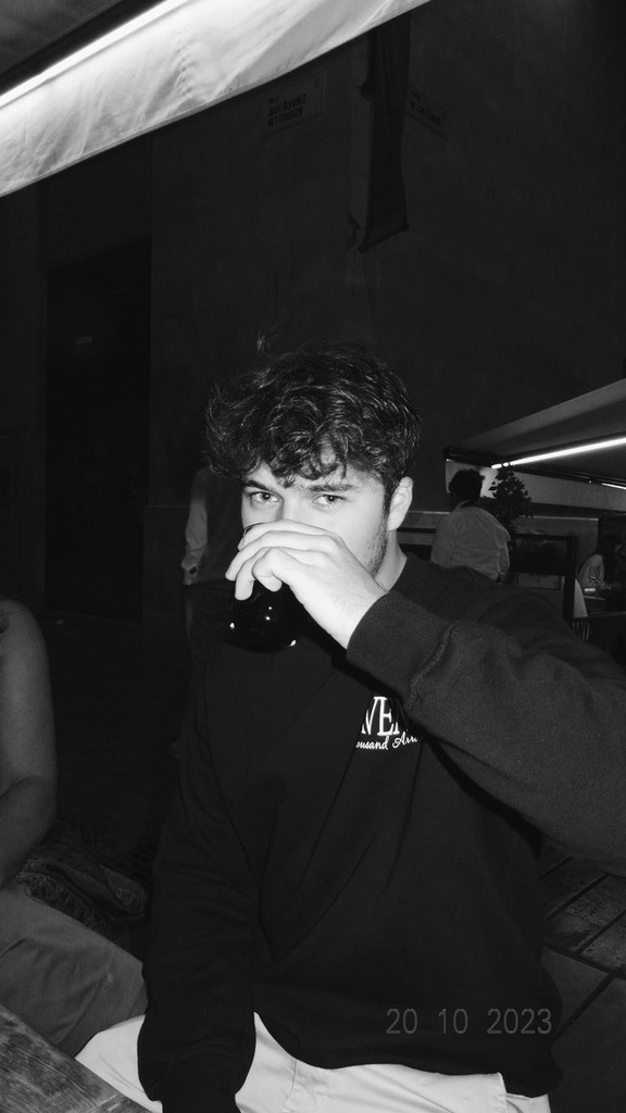 Close-up portrait of a person wearing a gray insulated hooded jacket with the hood up, showing their face framed by the hood against a light background.