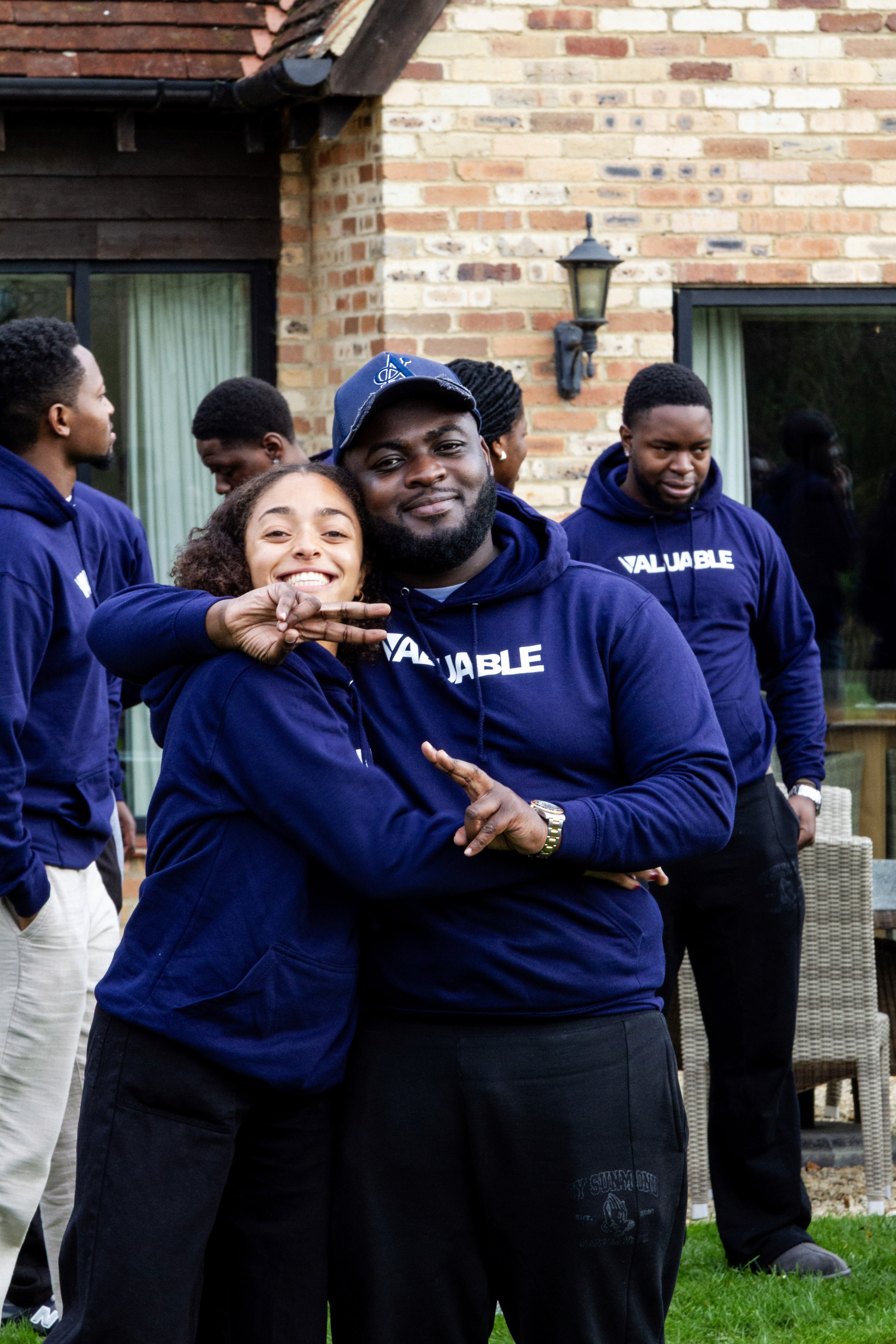 Two young people in matching blue valuable hoodies with "VALUABLE" text, smiling and posing for a photo outdoors.