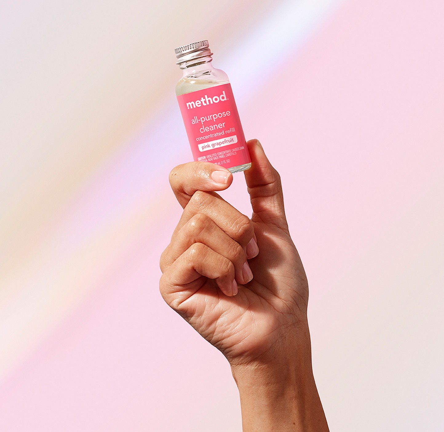 Hand holding up a small glass concentrate vial with a pink label against a pale pink backdrop