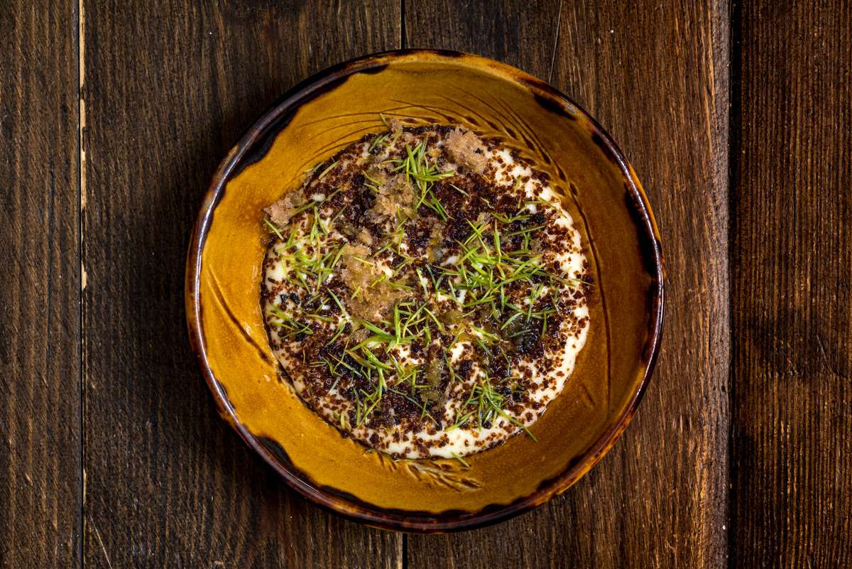 Top-down view of a yellow ceramic bowl filled with rice and topped with herbs and seeds on a dark wood table.