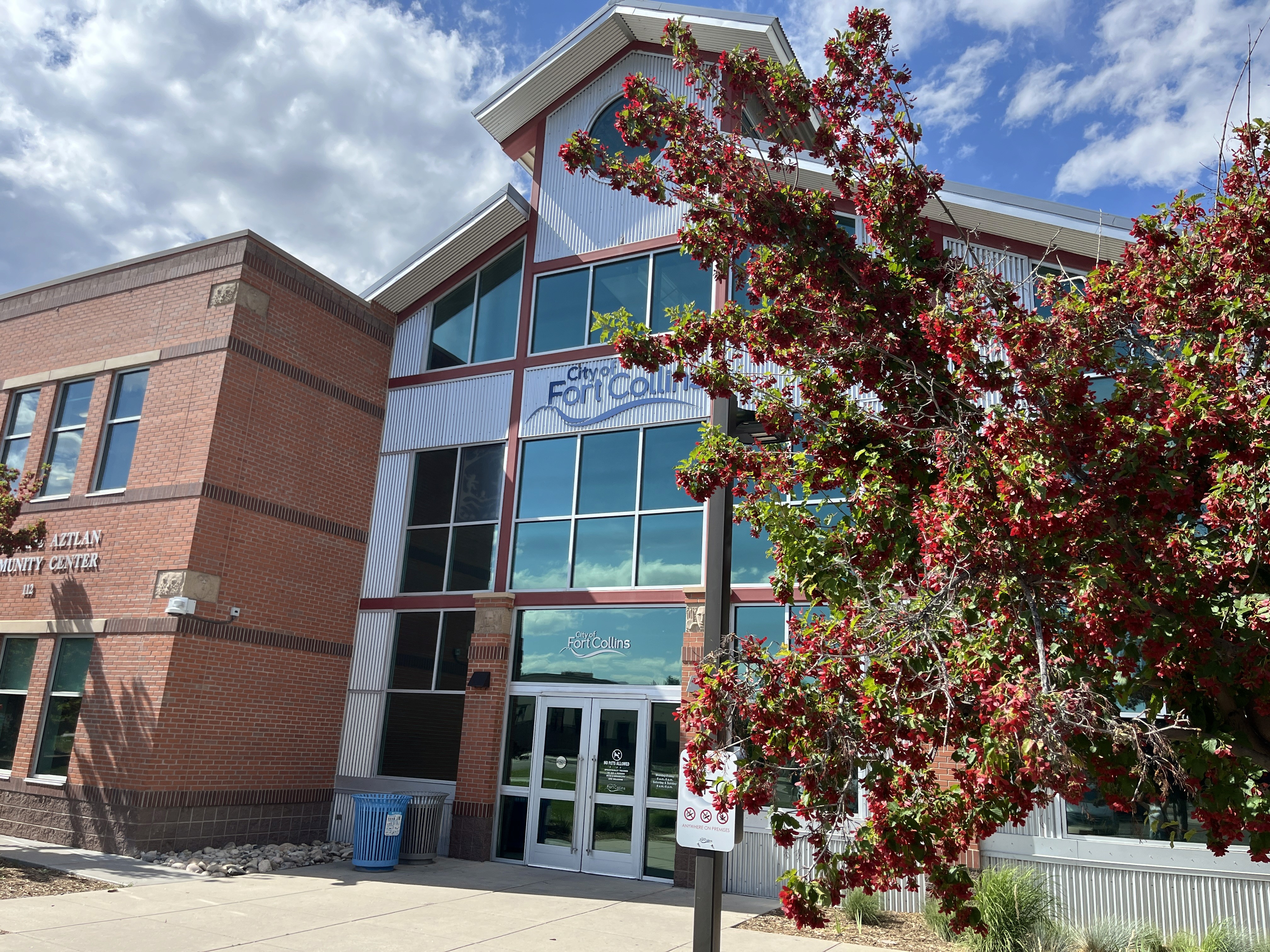 Northside Aztlan Community Center with red blooms on trees.