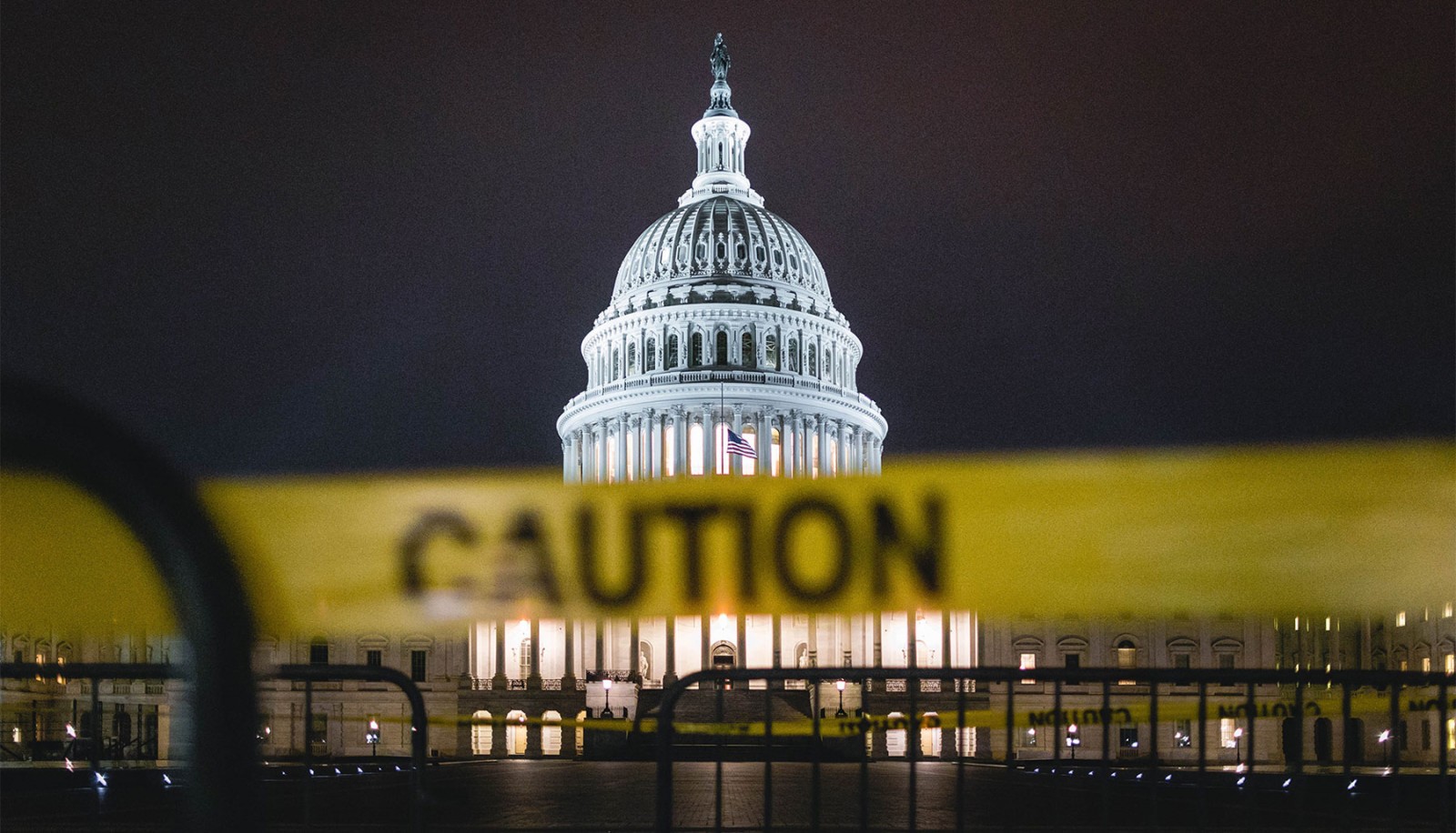 The U.S. Capitol is seen at night, with a large yellow "Caution" sign prominently displayed in the foreground.