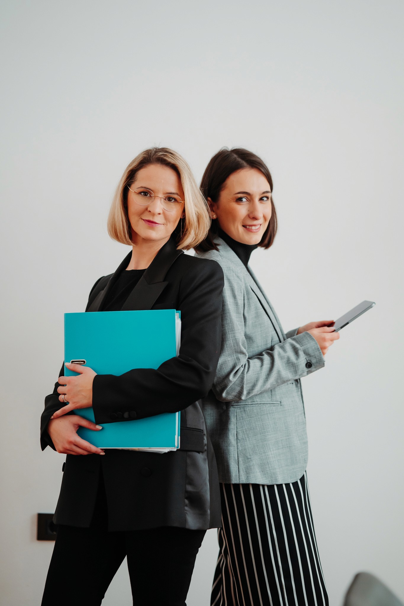 Modern open office lounge with large arched windows, plants, and soft round seating in white and terracotta tones, with people walking and working on laptops.