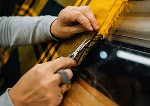 A close-up shot of a persons hand who is trimming with a scissor loose threads and inspecting a fabric in a light box