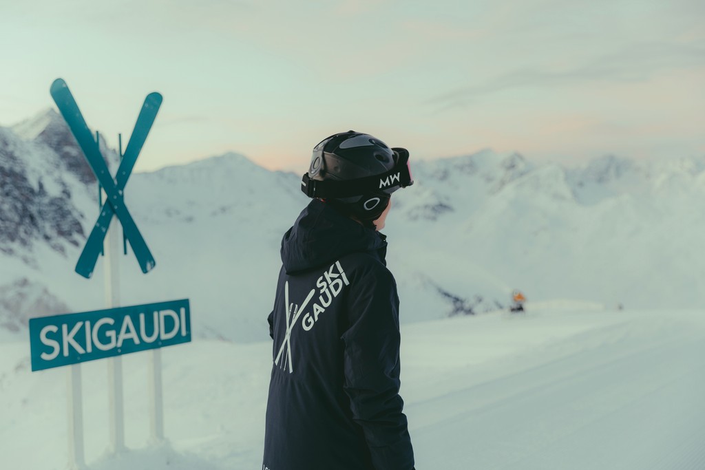 Person skiing in snowy mountains with Ski Gaudi sign visible.