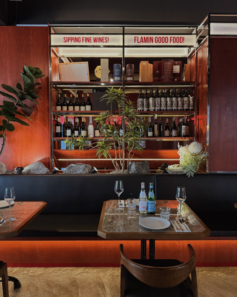 Interior of Fire Pitz steakhouse featuring elegant decor with a polished dining table, wine bottles on display, and lush greenery.