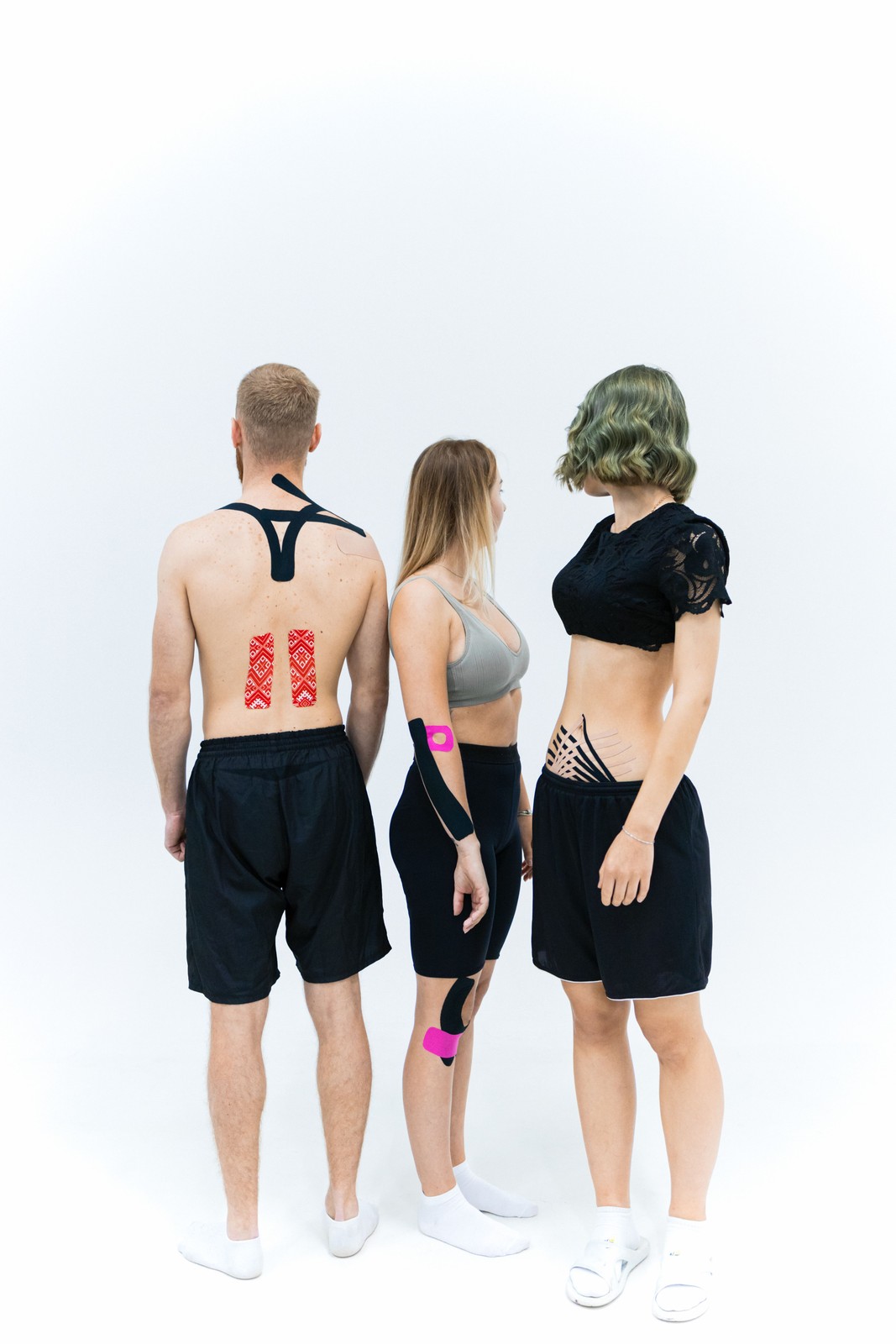 Three athletes standing together with kinesiology tape applied across their backs, shoulders and arms.