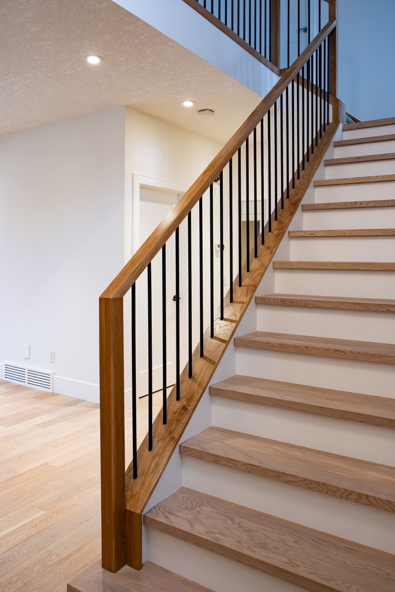 Image of Wooden staircase with black metal balusters and handrail in a modern home interior design by KHD Homes.