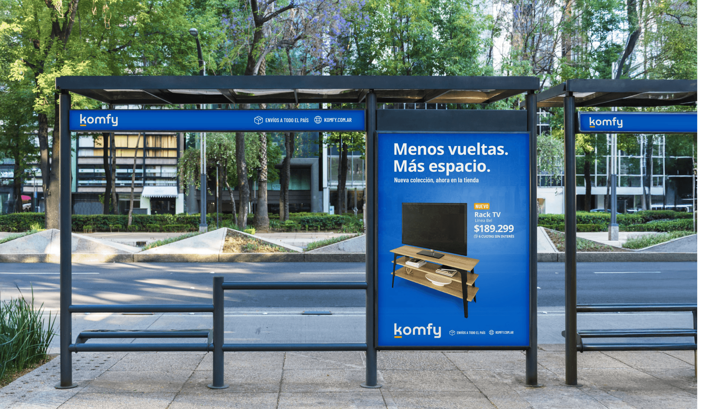 A modern outdoor bus stop features a blue advertisement for a "Rack TV" promoting space-saving storage, set against a backdrop of lush green trees and a quiet urban street.