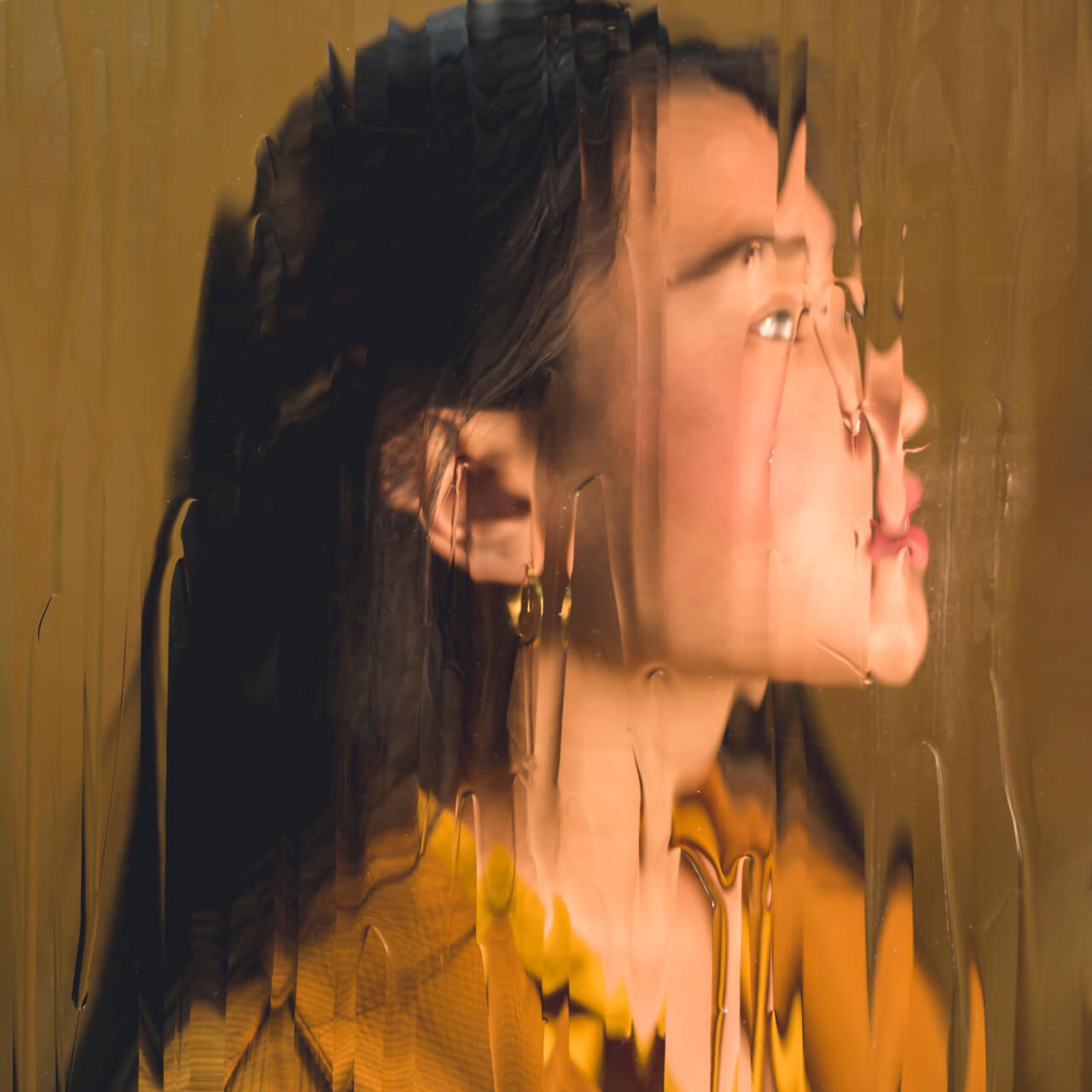 The image features a woman's face viewed through a rippled glass surface, creating a distorted, abstract effect against a warm, golden background.
