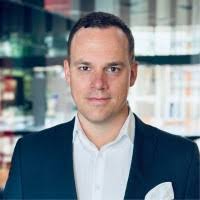 Business headshot of a confident Black woman smiling, wearing a turquoise blazer, with a minimal gray background