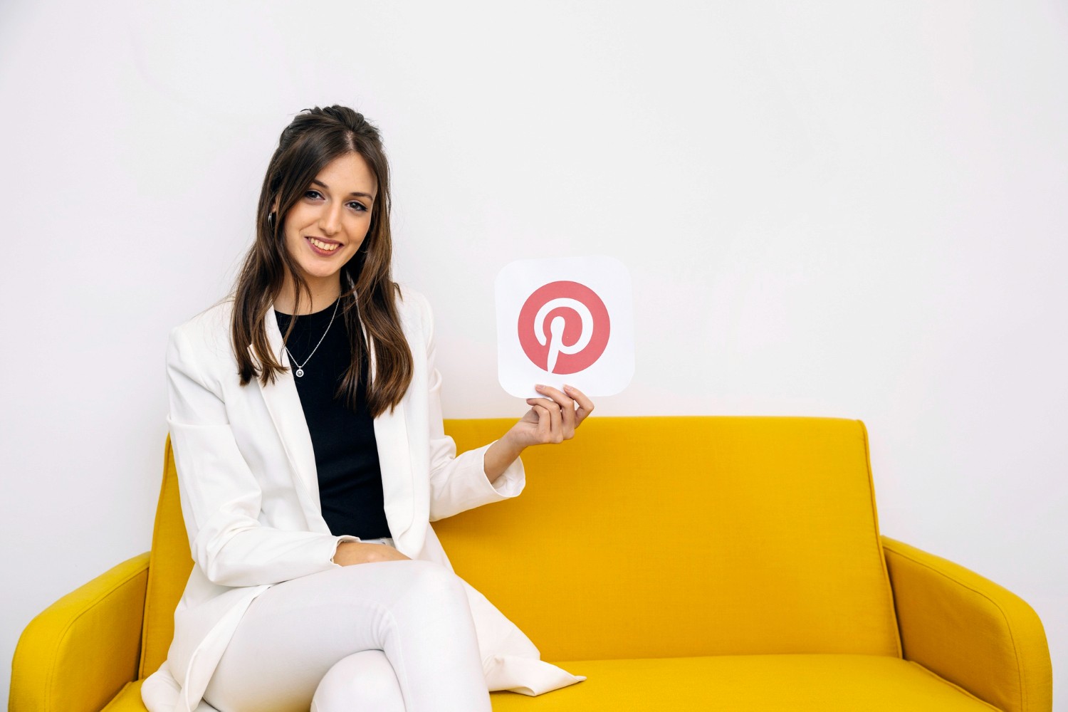  A woman seated on a couch, smiling while holding a Pinterest sign, showcasing her creativity and inspiration.