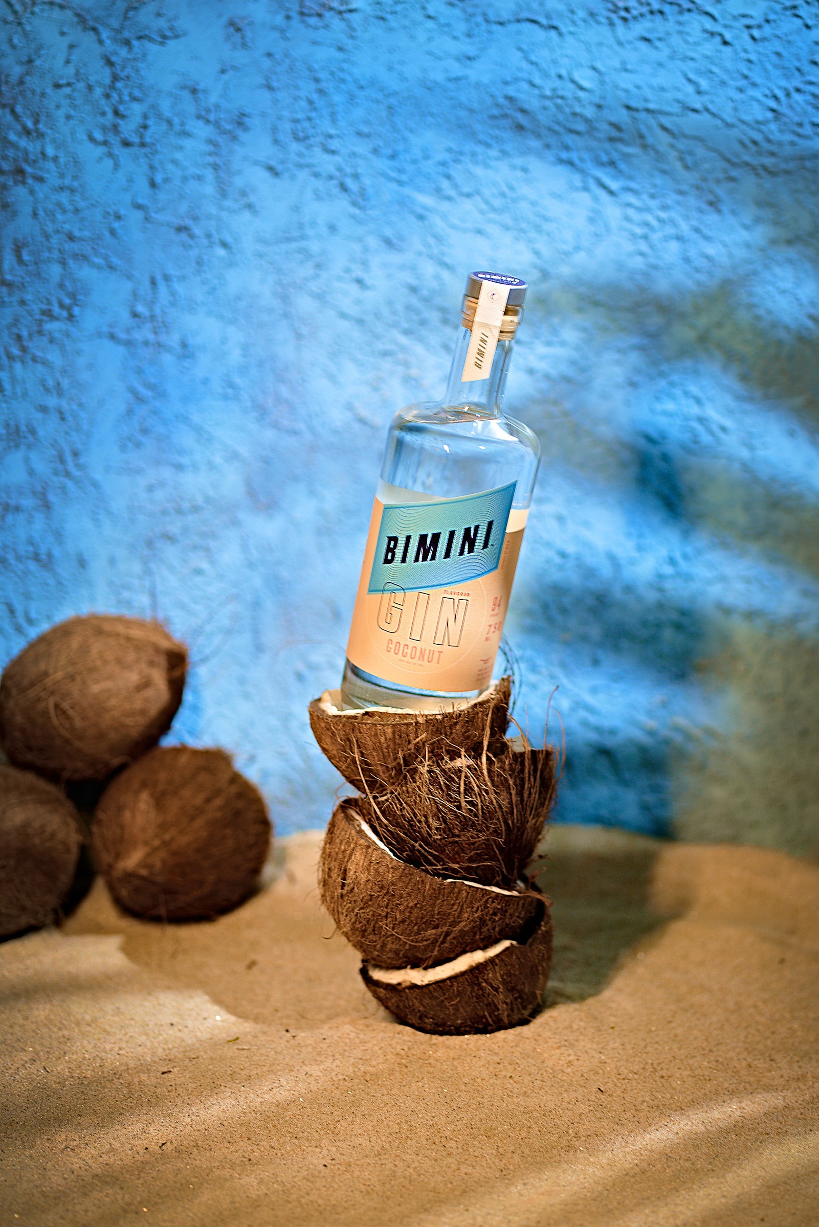 Bimini Gin bottle stacked with coconuts against blue sky and sand