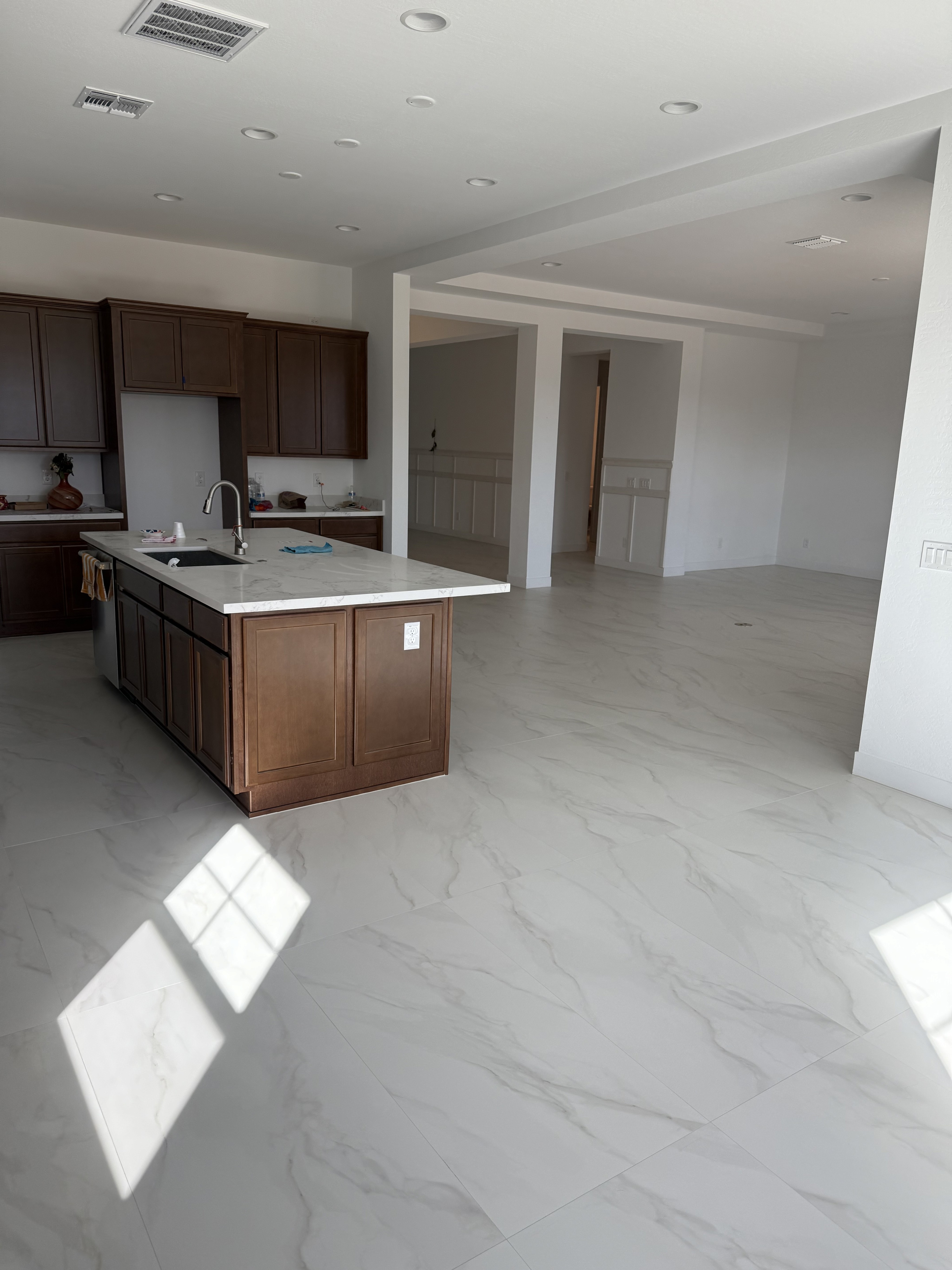Modern kitchen with wood-look tile flooring, dark cabinets, and construction materials in a new home under construction.