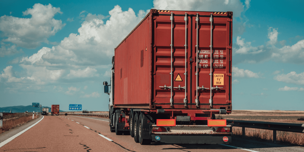 Rear view of a truck trailer hauling a red 40ft shipping container on an open highway.