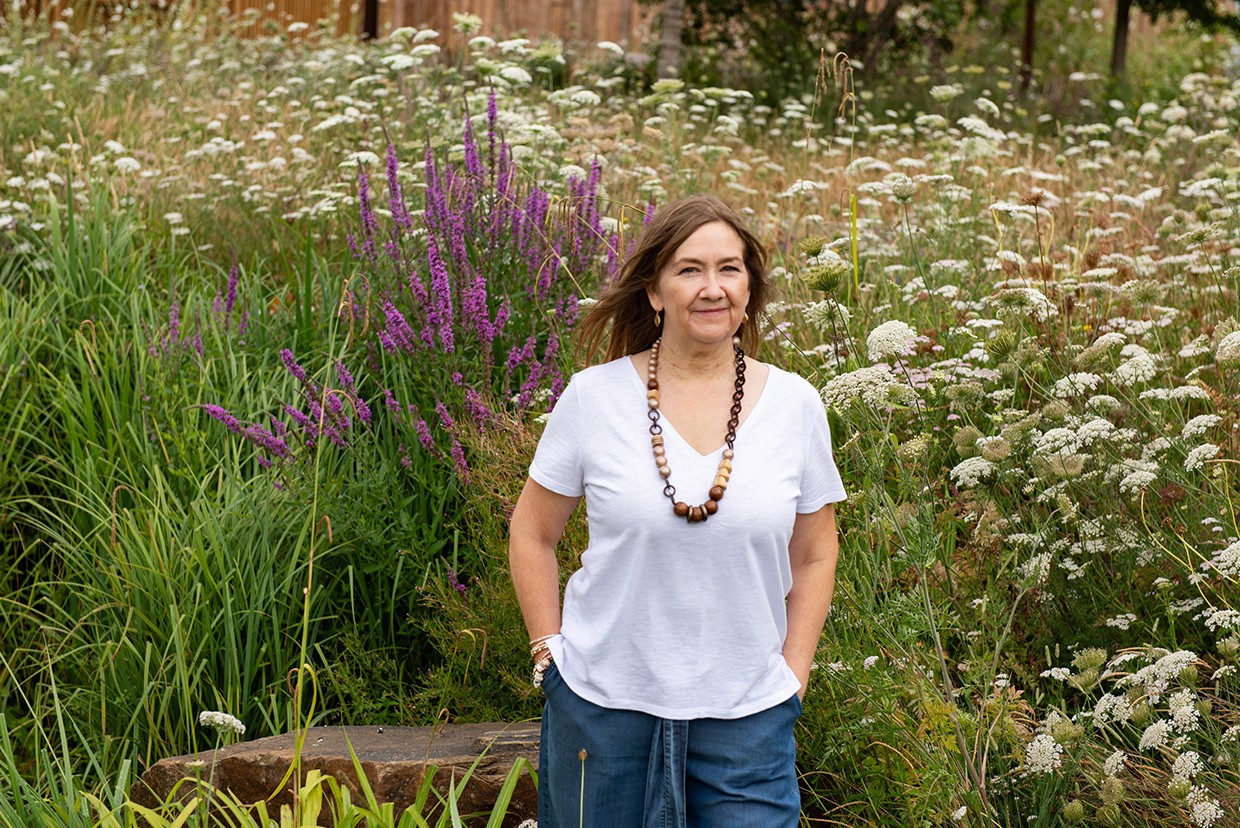 Mel in front of plants with white t-shirt smiling at the camera