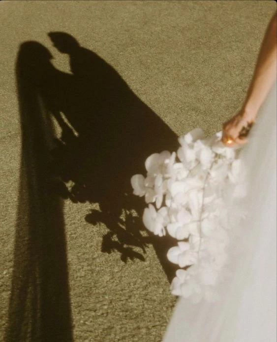 Fine art photograph of a bride holding a bouquet, with her shadow cast on the ground, creating an ethereal and artistic effect, photographed by Out of The Blues Fine Art Wedding Photography in Hyderabad.