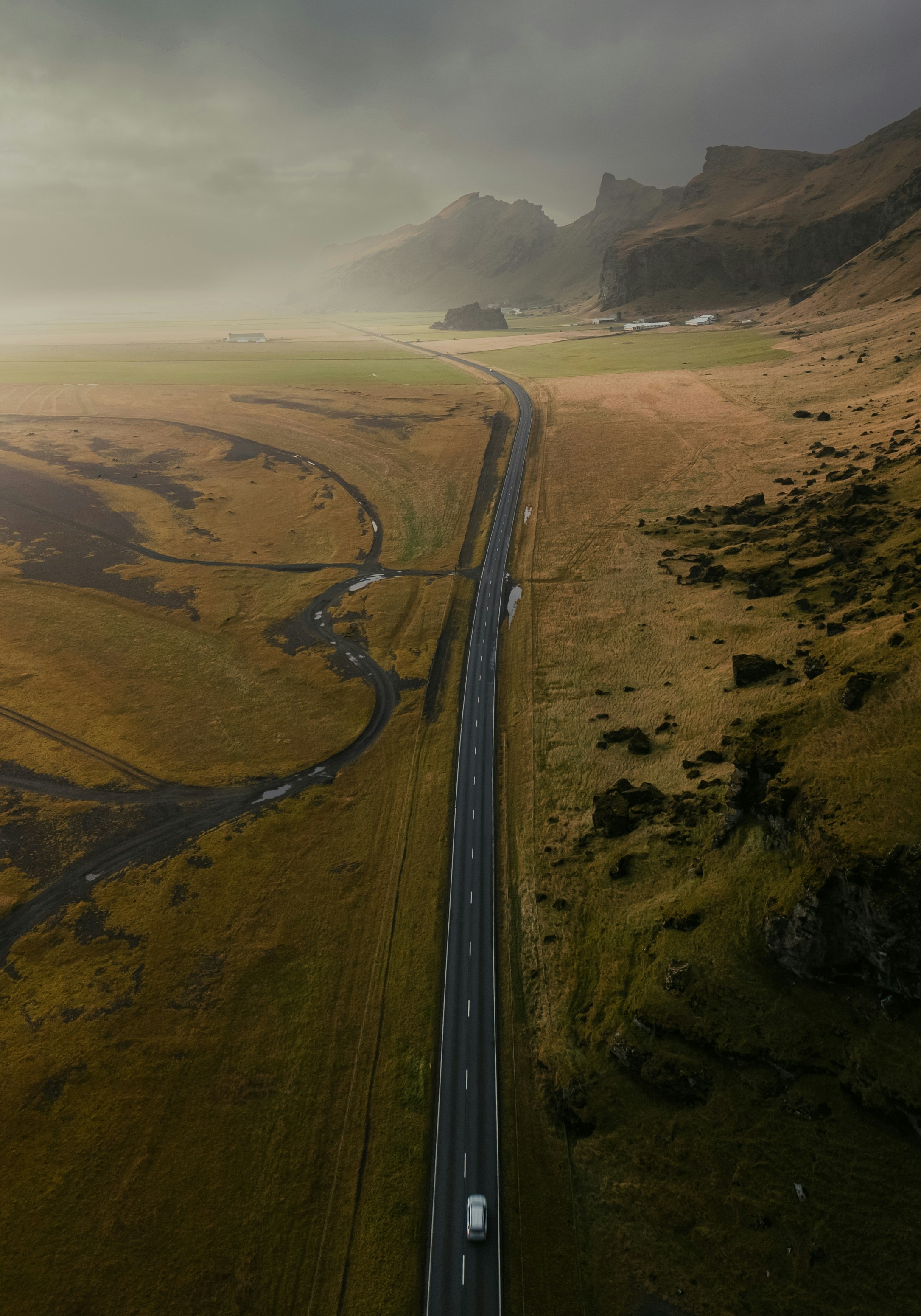 A lonely car drives on a long road through iceland.