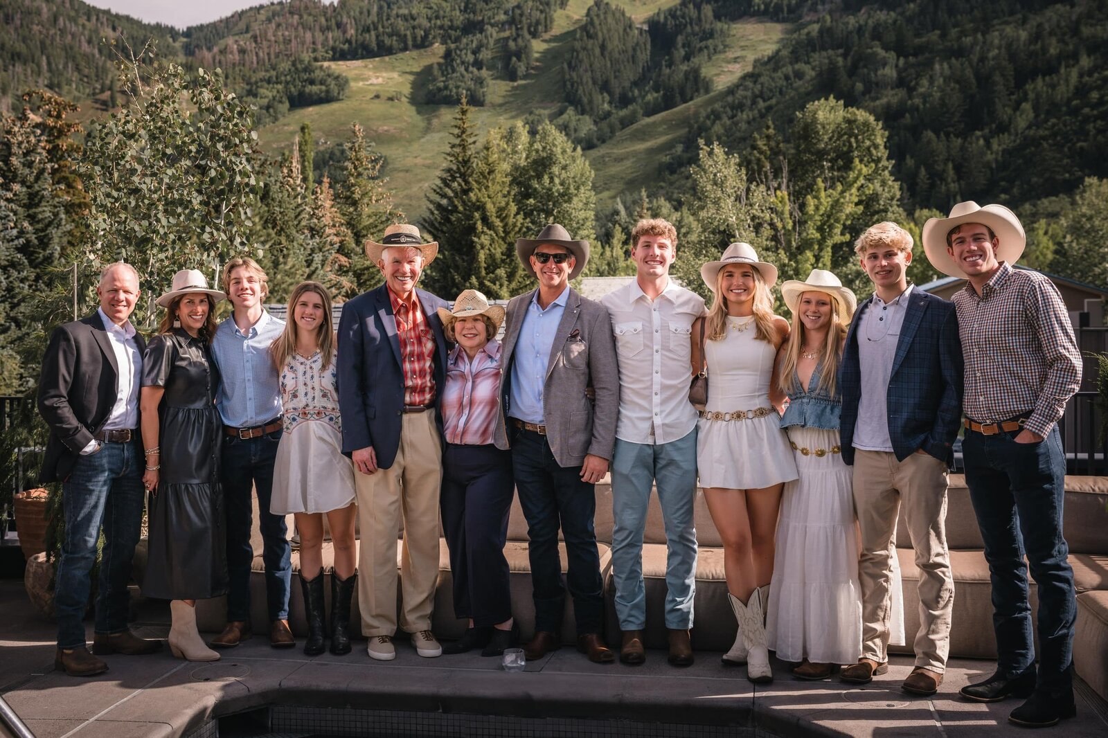 Guests in cowboy hats posing together on a terrace below wooded mountain slopes