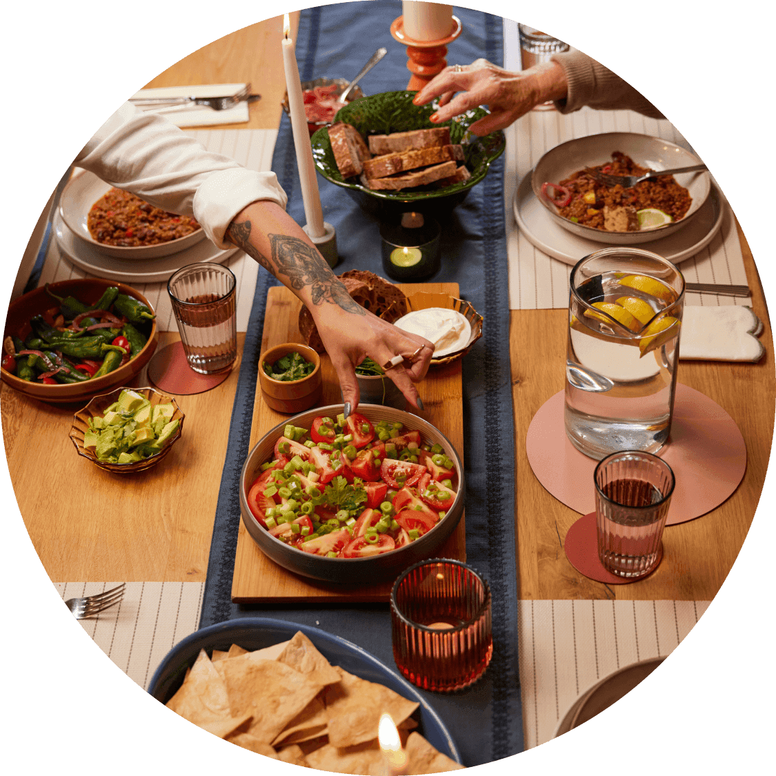 Hands reach across a dining table filled with shared dishes like salad, bread, and chips