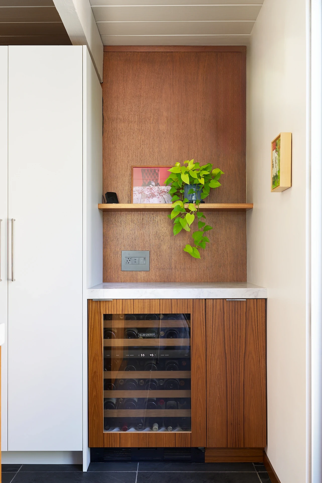 Portrait of the panel-ready wine fridge and bartop area, showcasing the blend of modern amenities and walnut cabinetry in the Eichler kitchen remodel. Photo by Todd Huge.