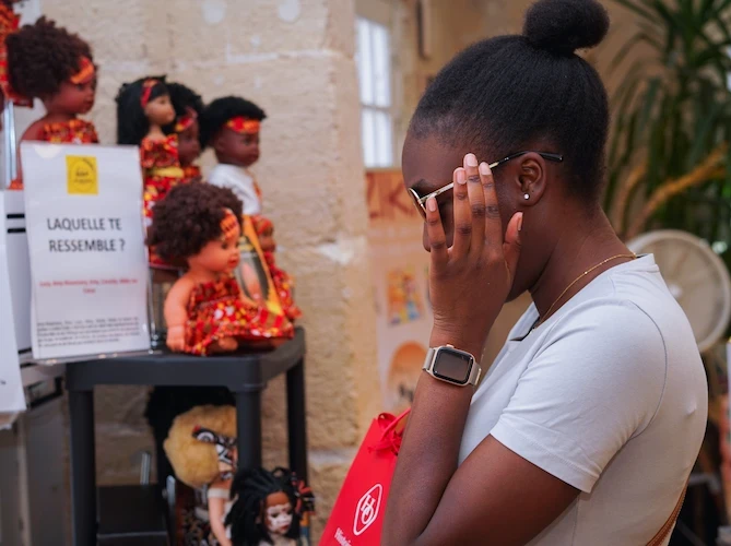 Visiteuse devant des poupées en tenues traditionnelles africaines lors d'un événement Douhomé