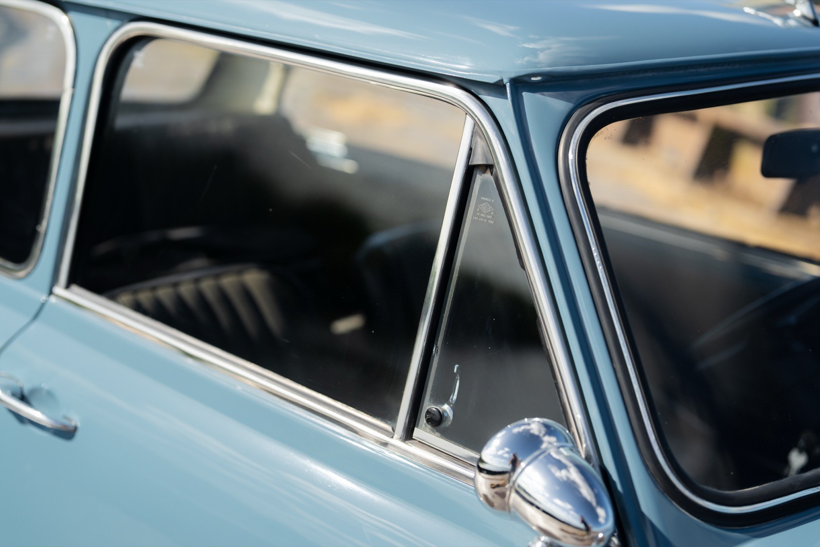 Close-up of a vintage car's window and interior, showcasing a light blue color and retro design.