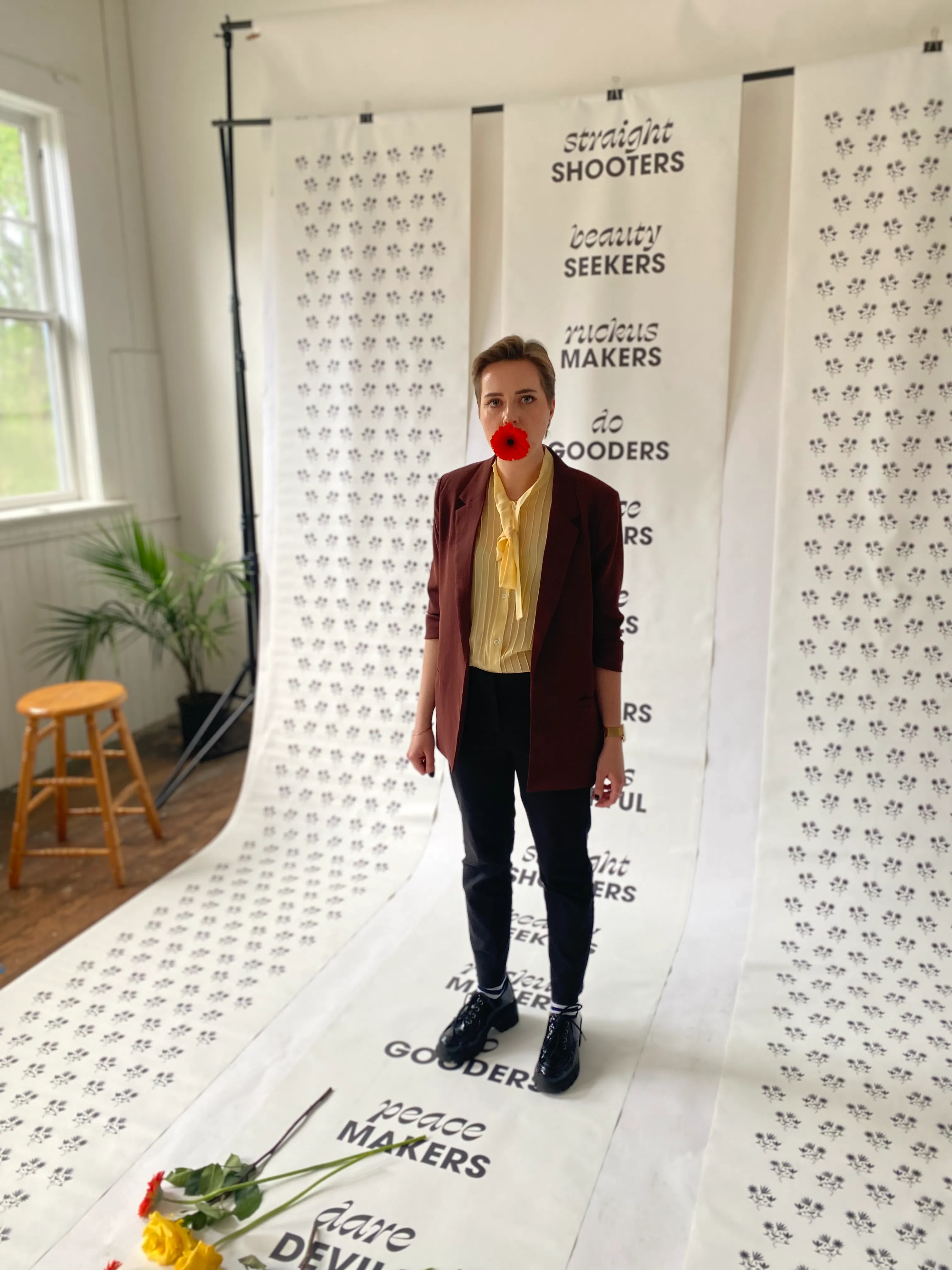 Emily Kiana standing in a photo studio on top of a Clever Jane backdrop that has various taglines written on it such as "truth seekers, ruckus makers, and tree huggers"