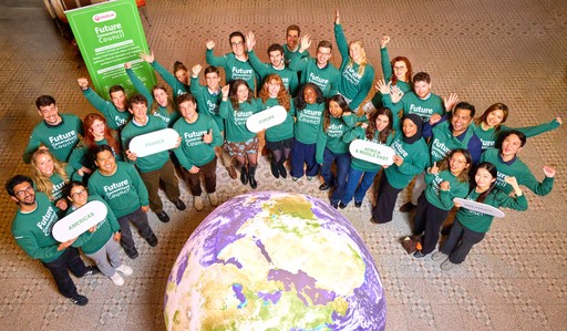 Smiling young man with short hair poses against a dark background, wearing a green button-up shirt.