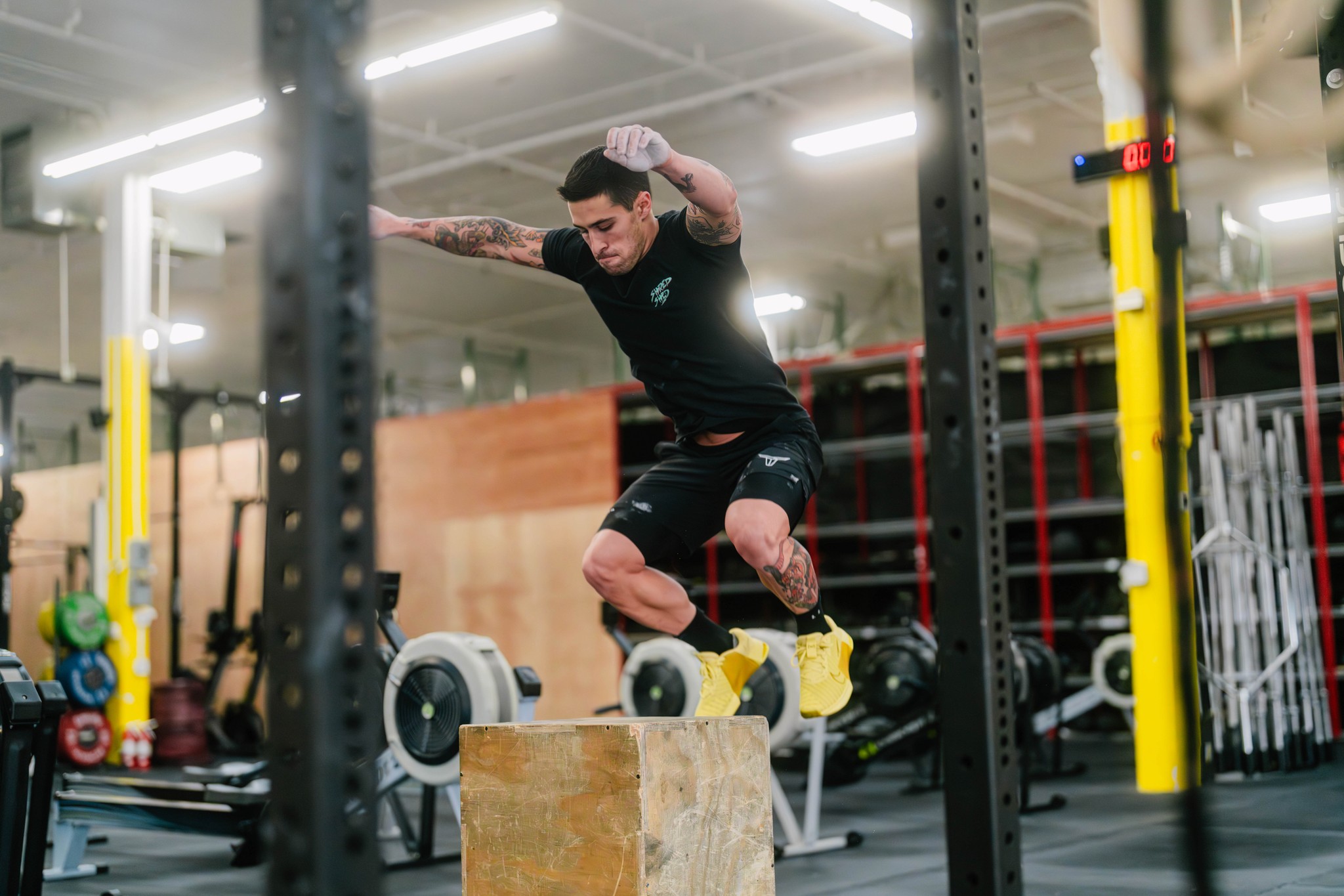 A male athlete mid-air during a box jump in a CrossFit gym, demonstrating explosive power and fitness.