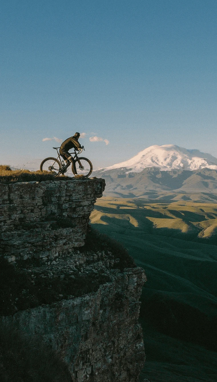 Cyclist riding a gravel bike on a rocky cliff with snow-capped mountain in the background