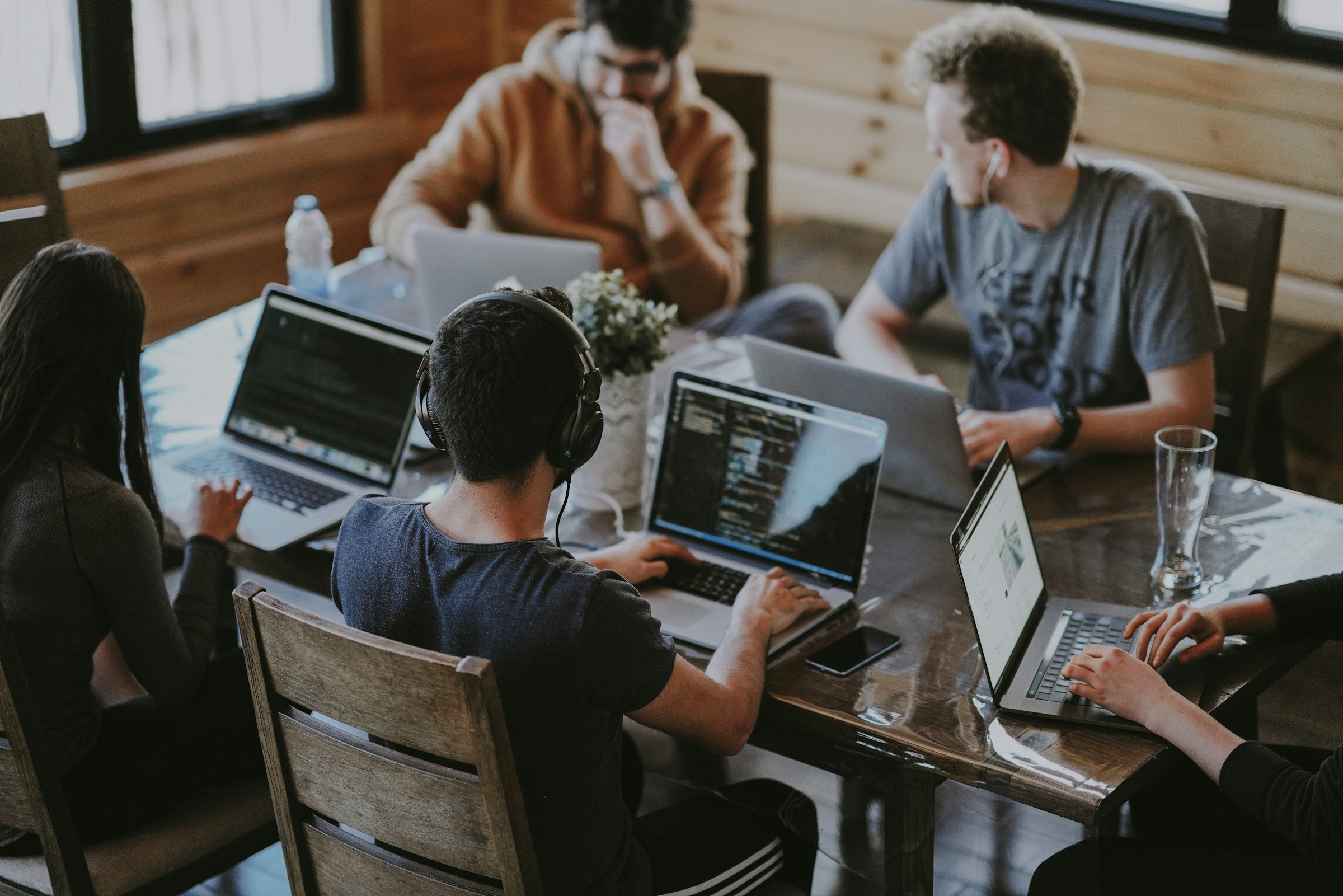 a group of people sitting around a table with laptops