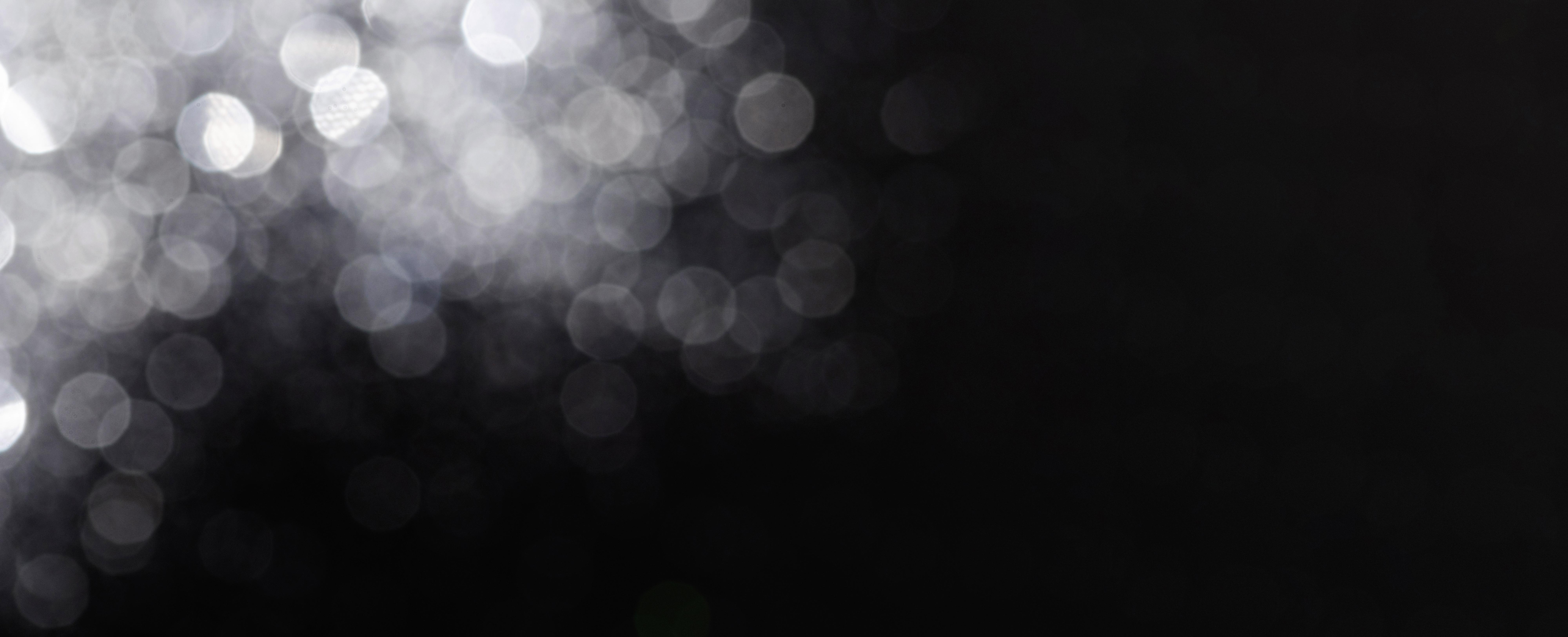 Abstract black and white image with blurred reflective glitter and bokeh lights on a dark background.