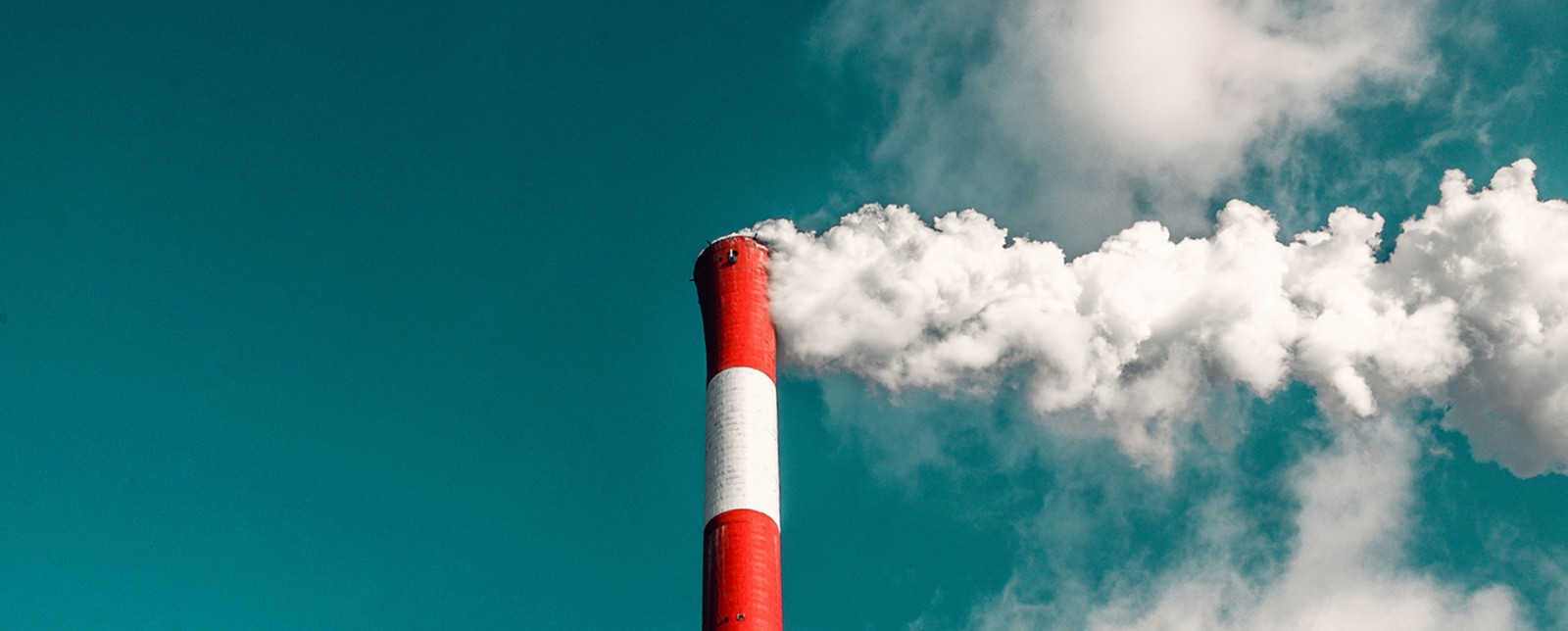 A red and white smokestack emits white clouds of smoke against a blue sky.