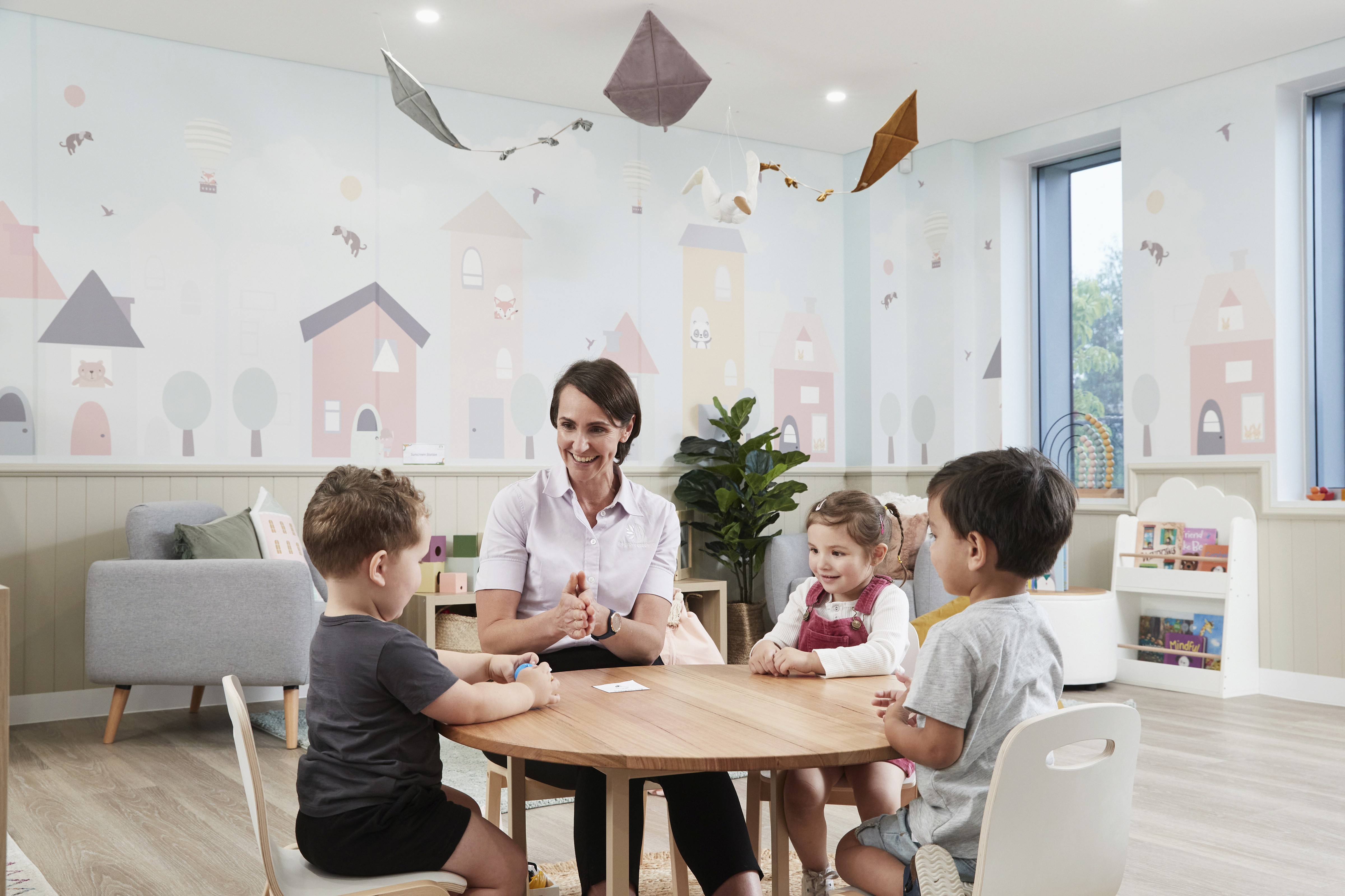 A smiling woman with her arms crossed, standing against a dark green background. She has long, dark hair.