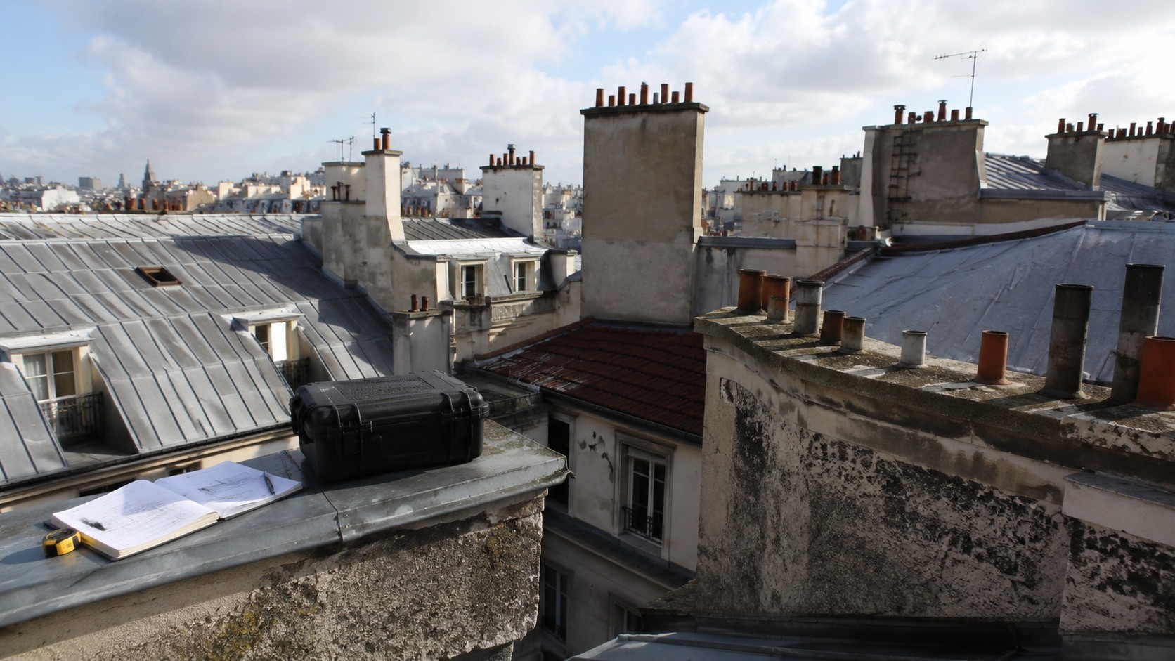 Vue de toitures parisiennes avec documents d’inspection et matériel d’audit pour évaluer l’état des couvertures d’un parc immobilier de foncière.