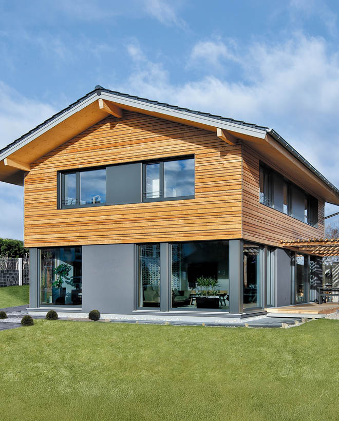 Modernes Holzhaus mit großzügigen Glasflächen, überdachter Terrasse und Grillstation, umgeben von einem gepflegten Garten.