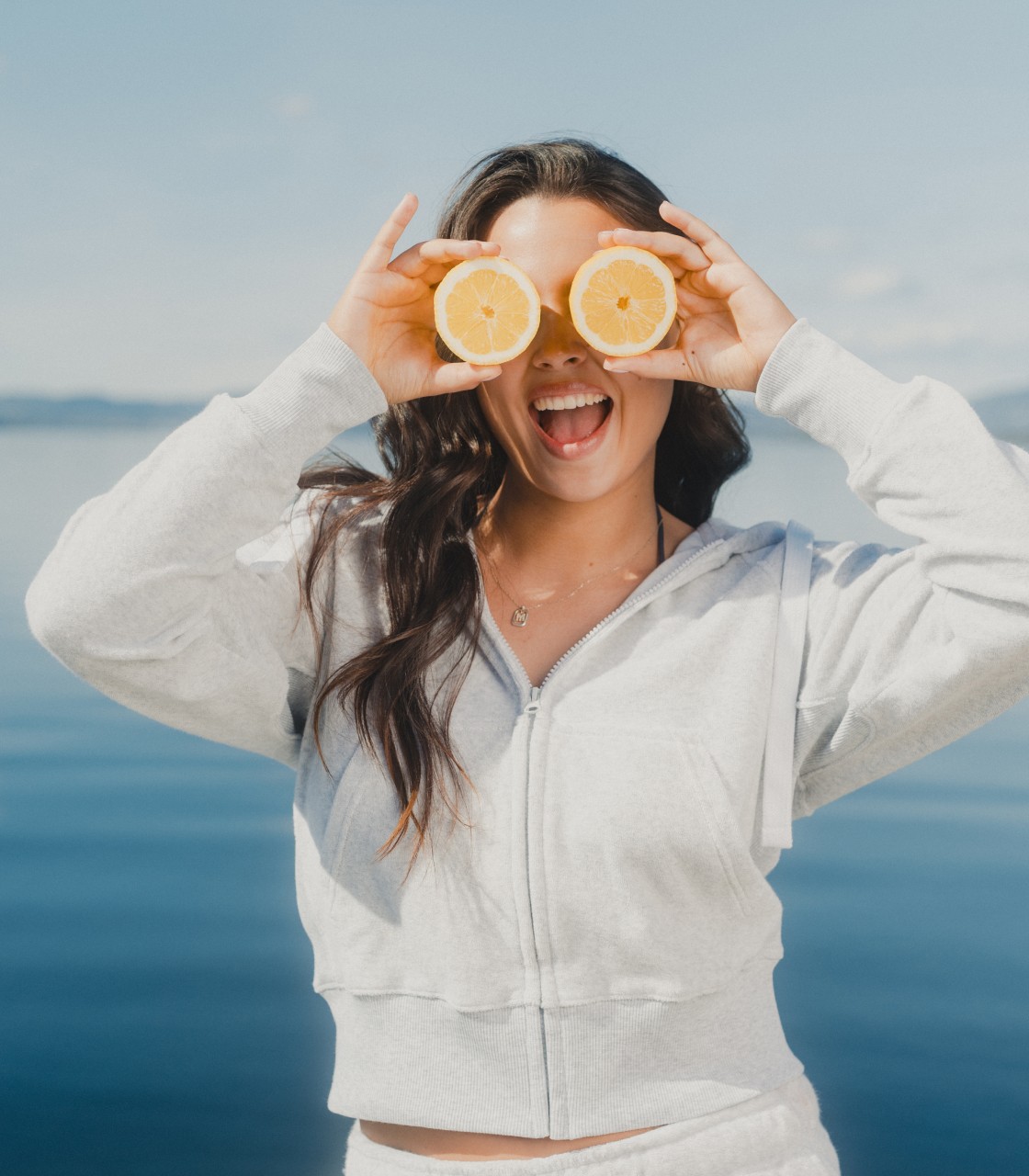 Woman in white hoodie covering eyes with lemon slices, casual clothing lifestyle photo