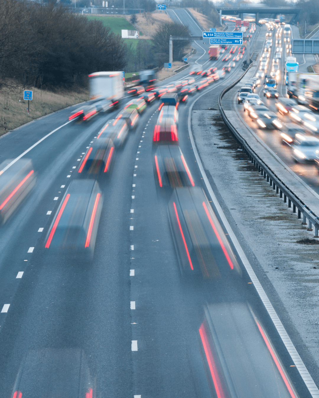 A smiling young man with crossed arms, wearing a plaid shirt and white t-shirt, poses against a dark background.