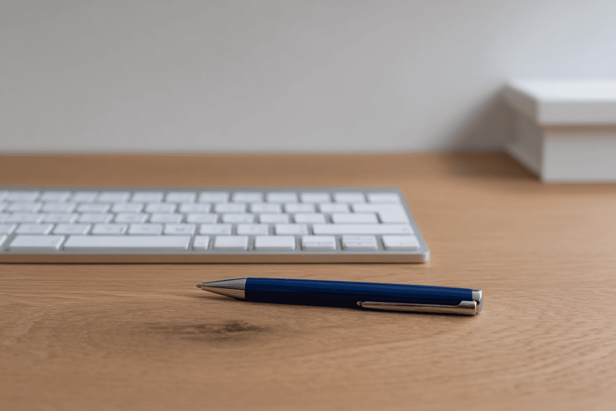 Pen on keyboard and notebook on white desk.