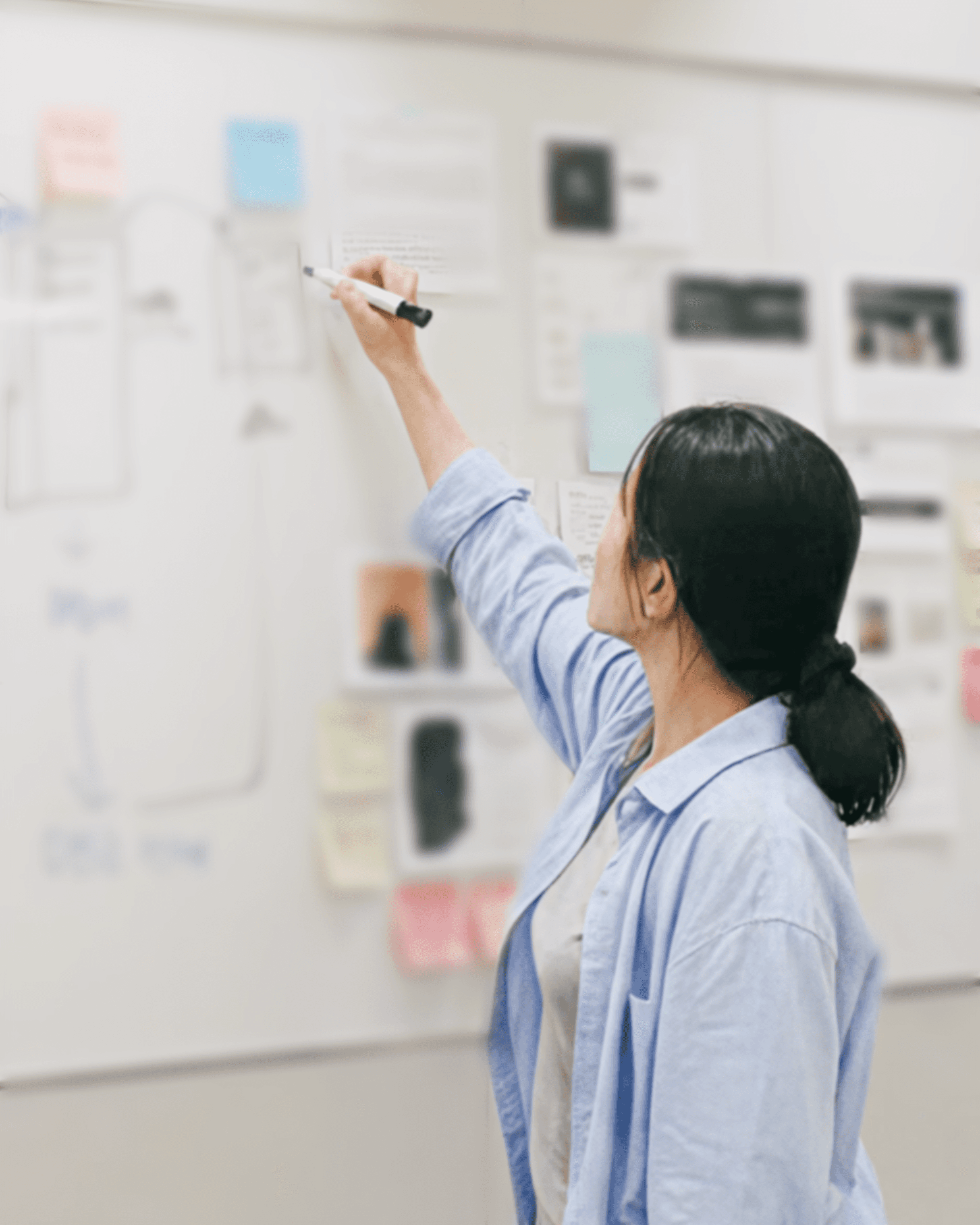 A person is writing on a whiteboard covered with notes and diagrams in a collaborative workspace.