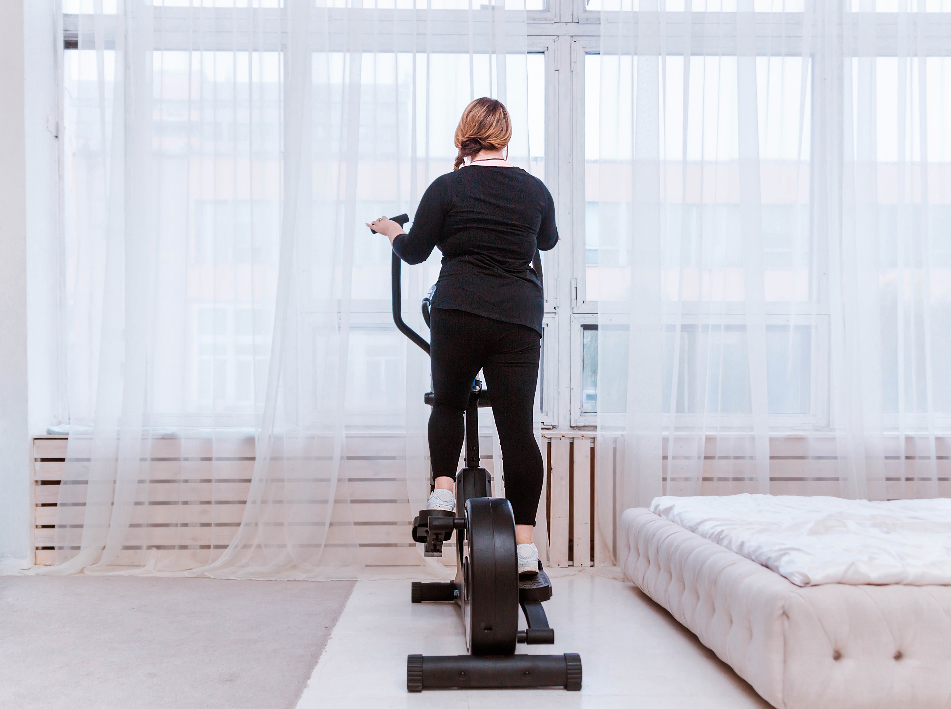 plus-sized woman doing a weight loss elliptical workout at home in her studio apartment