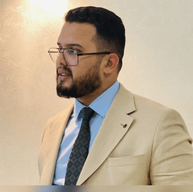 A young person with long, wavy hair sits in front of a plain background, looking directly at the camera.