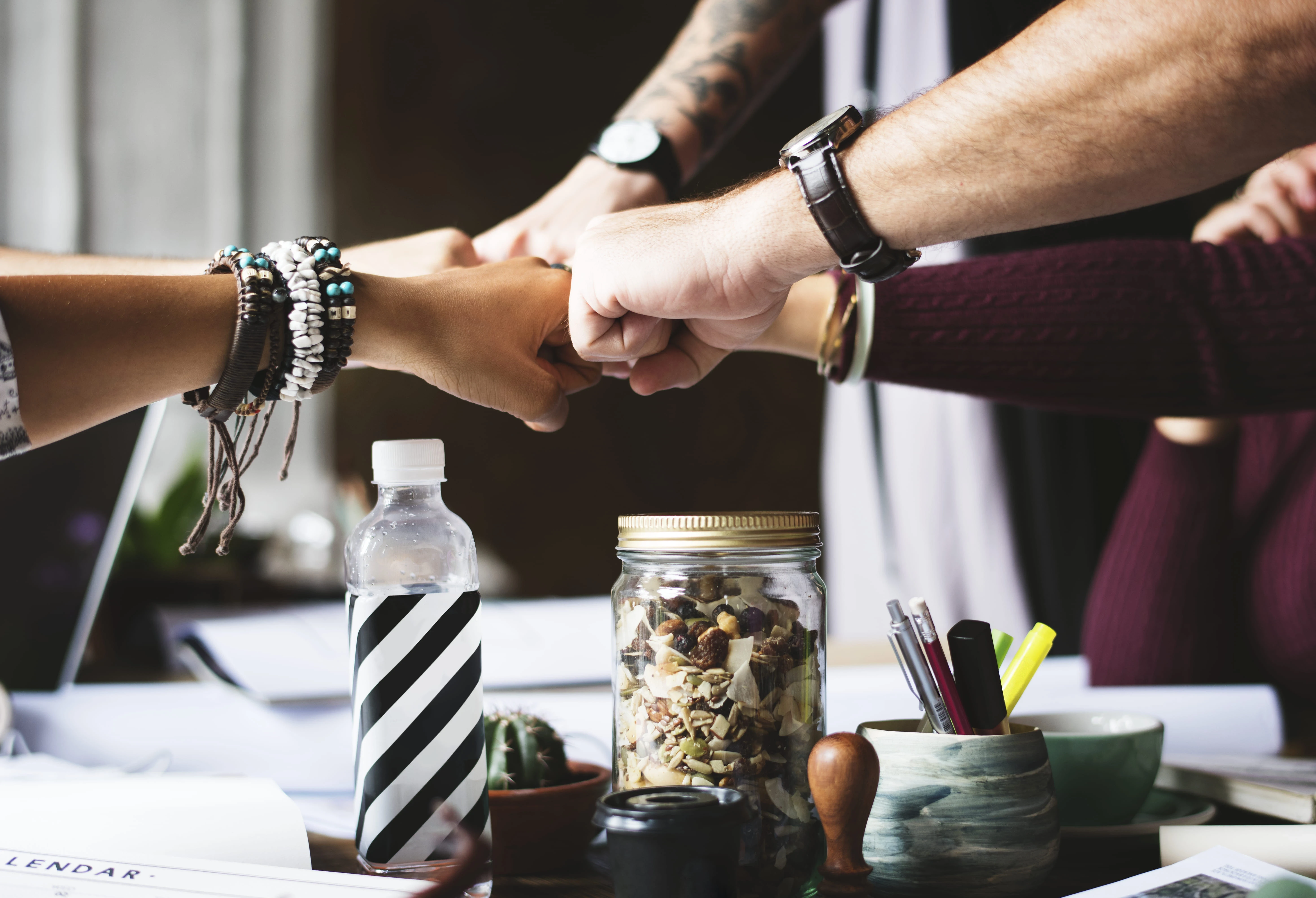 Team members bumping fists over a desk, symbolizing collaboration and teamwork in a shared workspace.