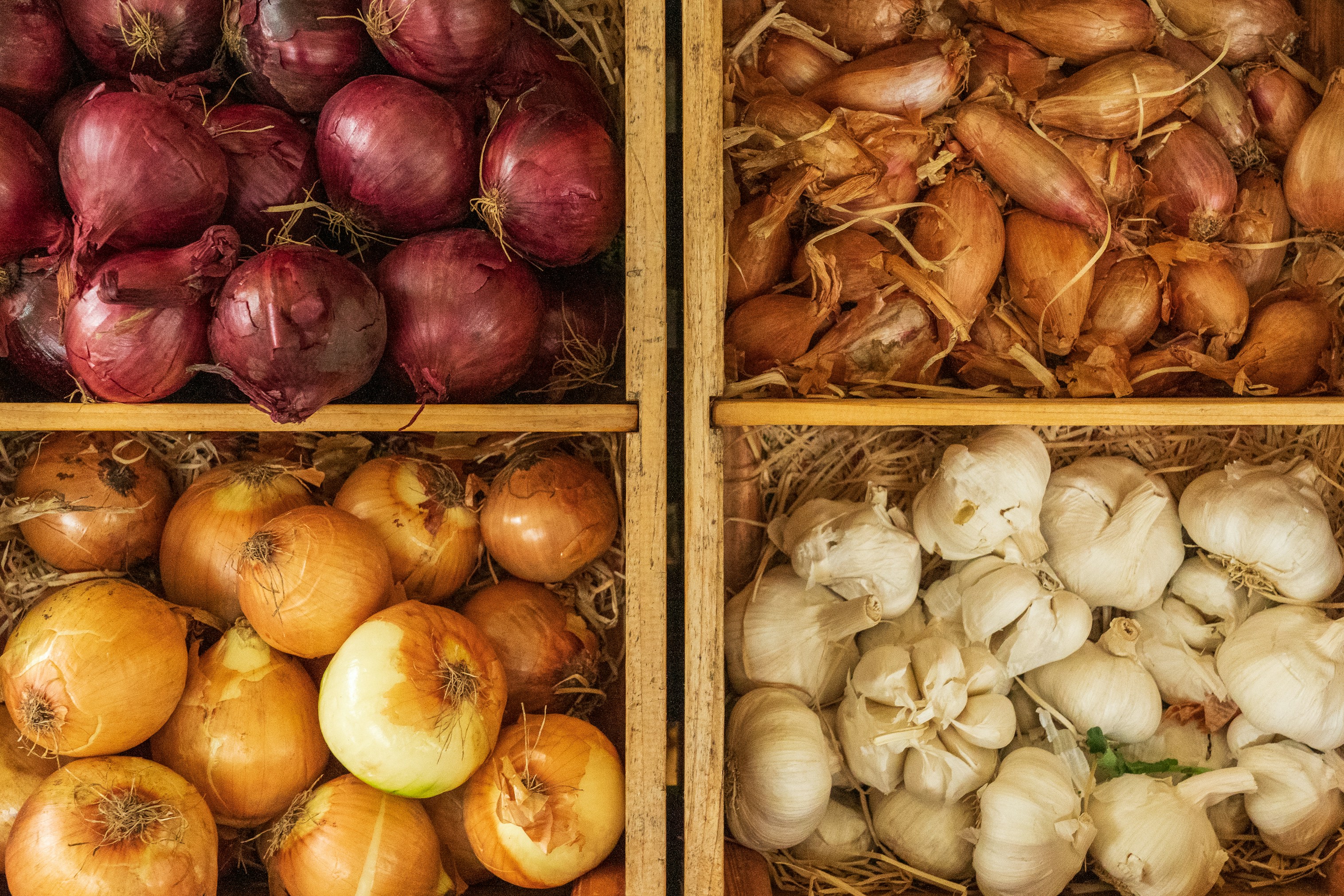 Wooden crates of red onions, shallots, brown onions and garlic, high-FODMAP foods often limited during the SIBO elimination phase