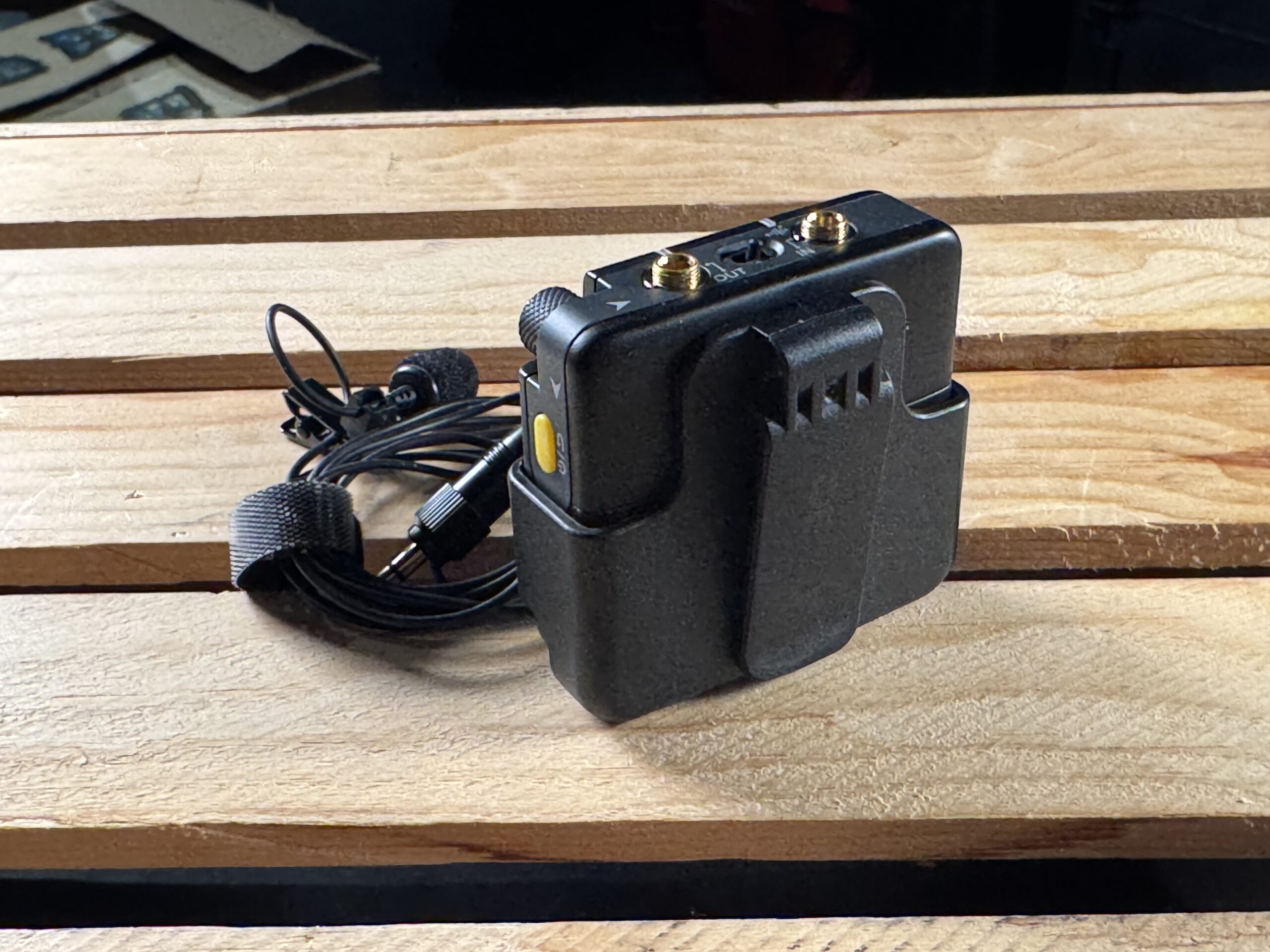 The rear view of a pocket audio recorder inside its plastic belt clip housing on a wooden surface.