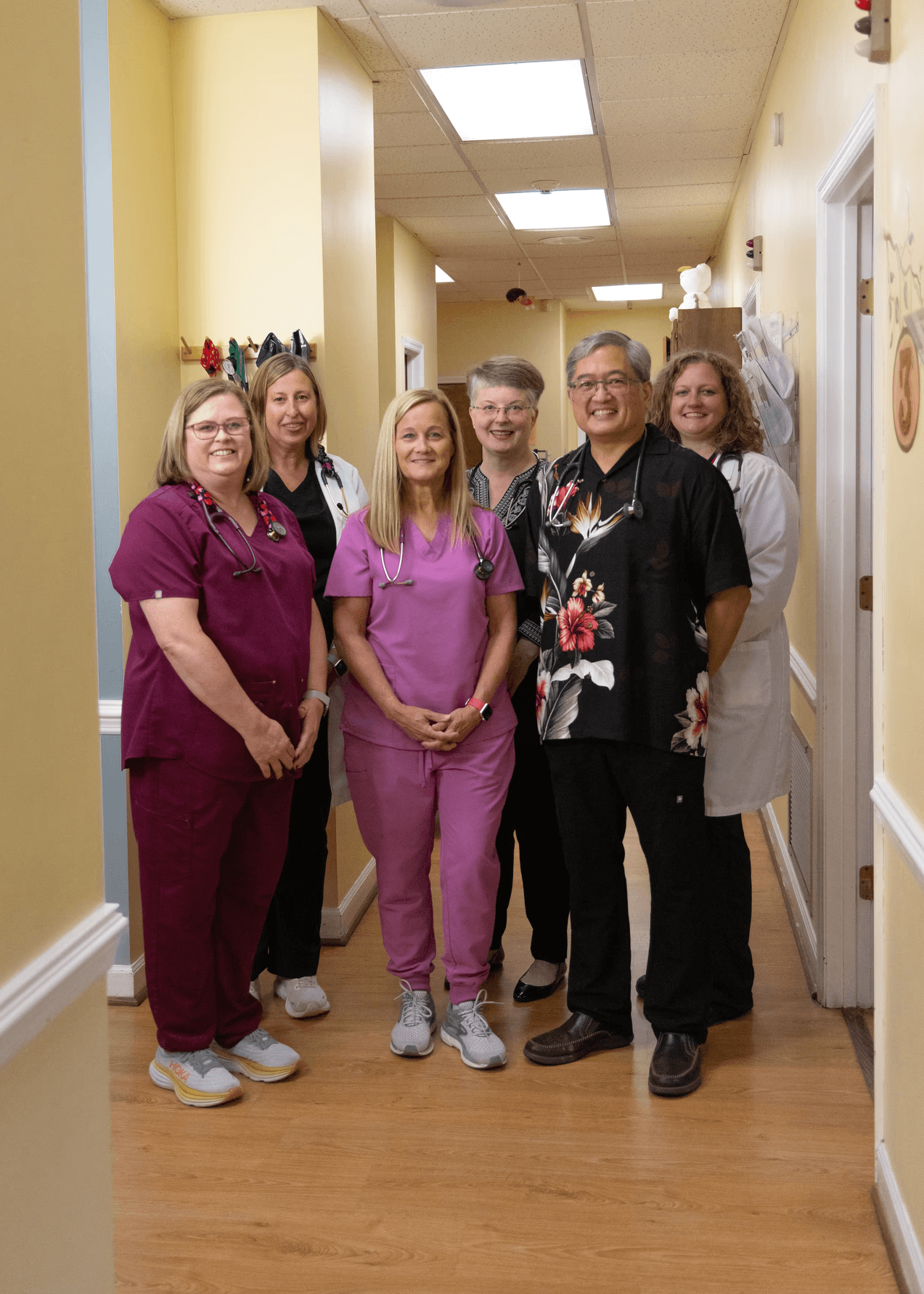 Team of six Pediatricians and Nurse Practitioners standing and smiling in their hallway.