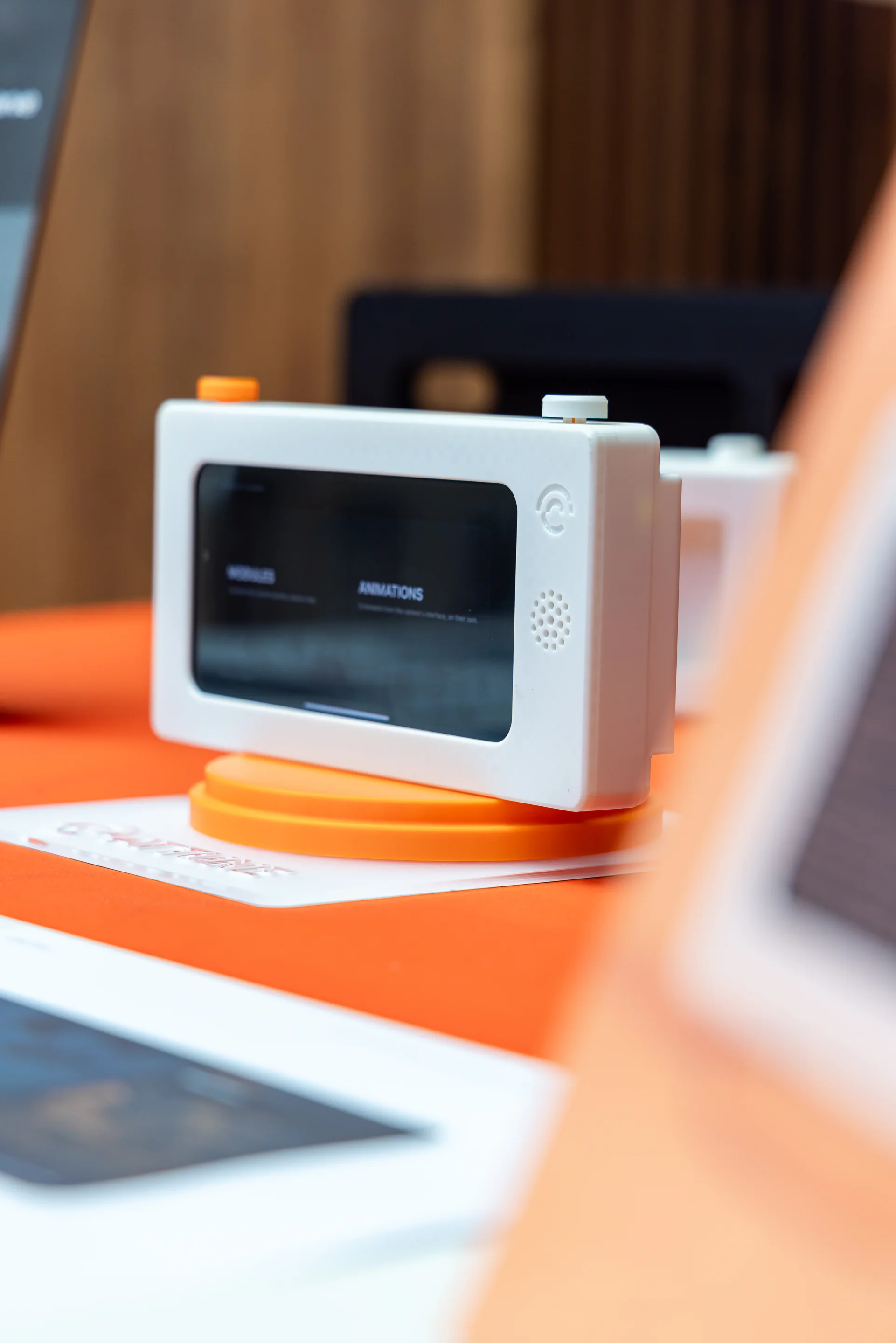 Close view of the white camera prototype on an orange display base, with its screen and controls visible.