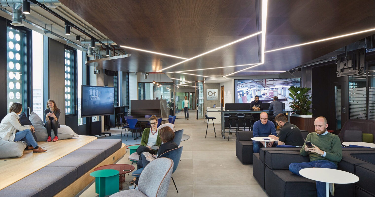 Modern home office setup with a monitor, ergonomic chair, keyboard, and indoor plants near a window with blinds.