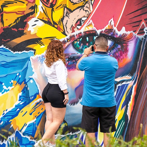 两个人站在色彩斑斓的涂鸦墙前，其中一个正用智能手机拍照。